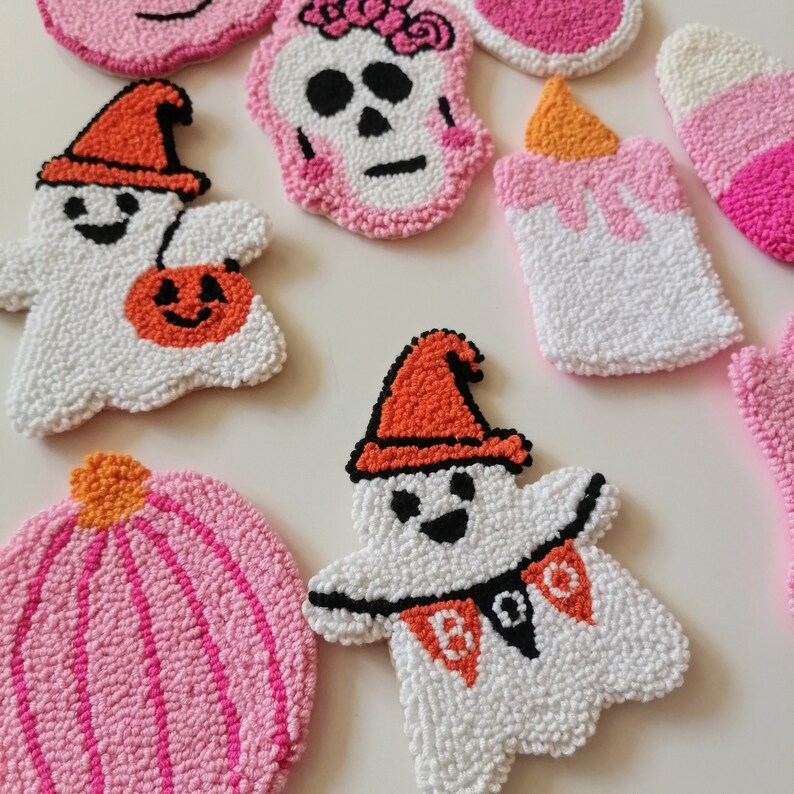 May include: A set of nine Halloween-themed felt ornaments. The ornaments are shaped like ghosts, pumpkins, a skull, and a candle. The ornaments are all white with pink and orange accents.