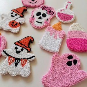 May include: A set of nine Halloween-themed felt ornaments. The ornaments are shaped like ghosts, a skull, a bottle, a candle, and a candy cane. The ornaments are all pink and white with black accents.
