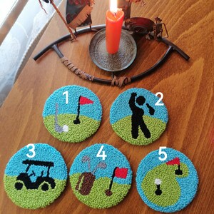 以下が含まれることがあります： ゴルフをテーマにしたデザインの、手作りの丸いコースター5枚。各コースターは、青い空の背景、緑の芝生、旗、ゴルファー、ゴルフカート、ゴルフバッグなど、ゴルフに関連する画像が特徴です。コースターには1から5までの番号が付けられています。