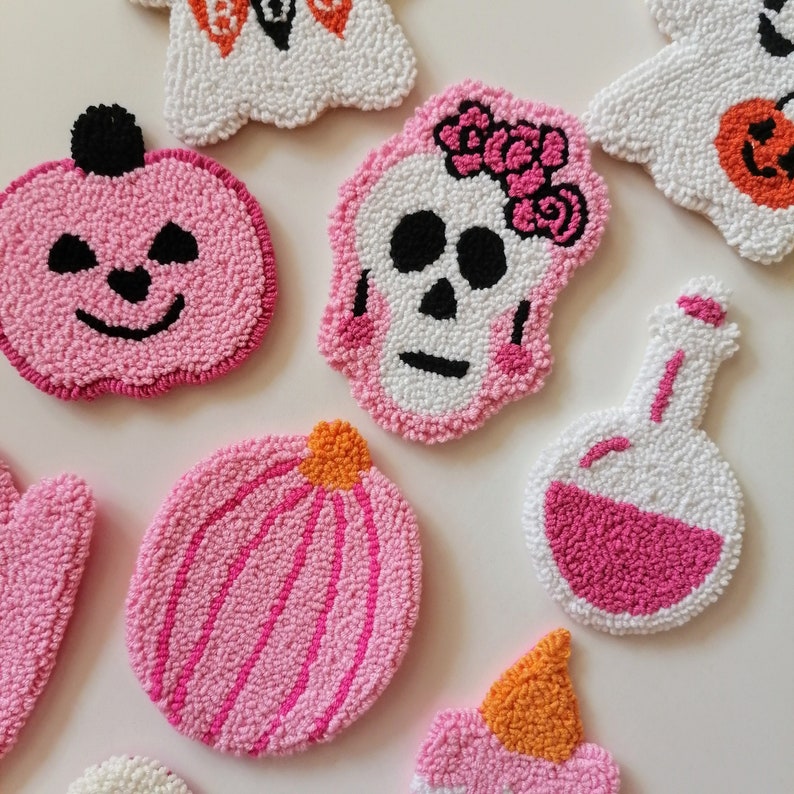 May include: A set of eight pink and white felt Halloween-themed ornaments. The ornaments are shaped like a pumpkin, a skull, a ghost, a potion bottle, and a witch's hat.