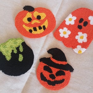K&ouml;nnte beinhalten: Vier Halloween-Motive aus Filz. Eines ist ein K&uuml;rbis mit einem schwarzen Hut, ein anderes ist ein K&uuml;rbis mit einem schwarzen Gesicht, ein weiteres ist ein Geist mit wei&szlig;en Blumen und das letzte ist ein gr&uuml;ner und schwarzer Geist.