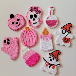 May include: A set of ten pink and white felt Halloween ornaments. The ornaments include a ghost, a pumpkin, a skull, a potion bottle, a candle, a candy cane, and two ghosts with the text "BOO" on them.