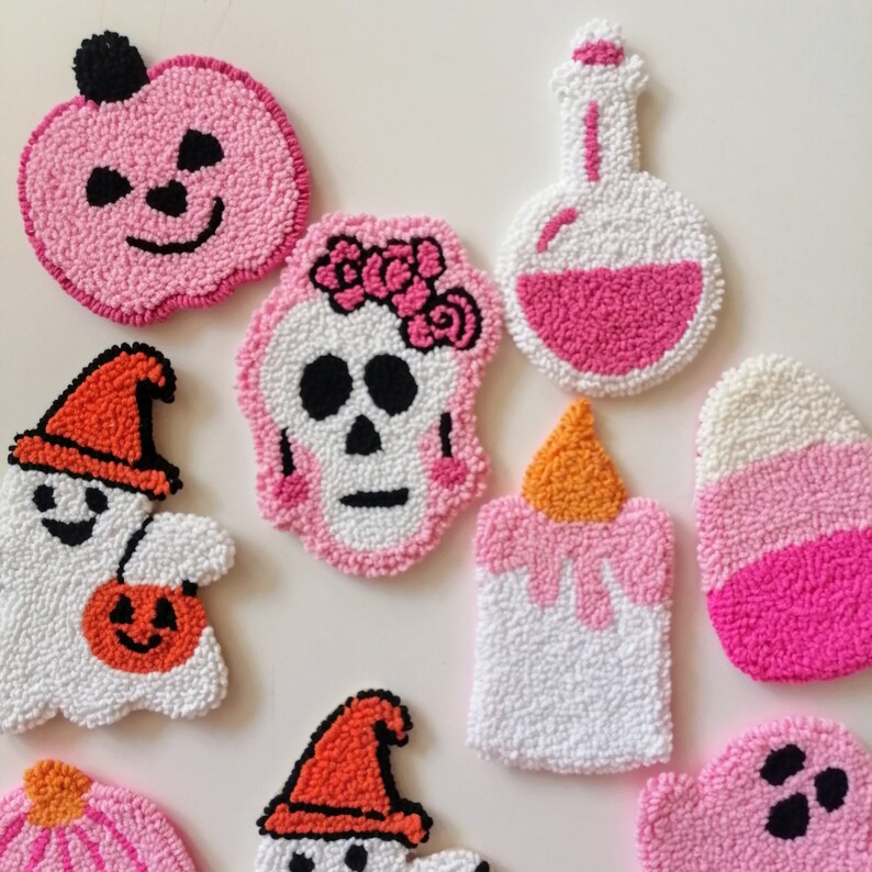 May include: A set of nine Halloween-themed felt ornaments. The ornaments are in various shapes, including a ghost, a skull, a pumpkin, a candle, and a potion bottle. The ornaments are all white with pink and orange accents.