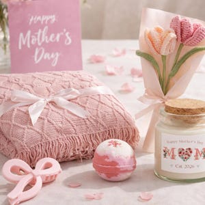 Könnte beinhalten: Ein rosa Geschenkset zum Muttertag, bestehend aus einer Decke, einem Strauß gehäkelter Tulpen, einer Kerze, einer Badekugel und einer Karte. Auf der Karte steht "Happy Mother's Day". Das Kerzenetikett lautet "MOM" und "Est. 2020".