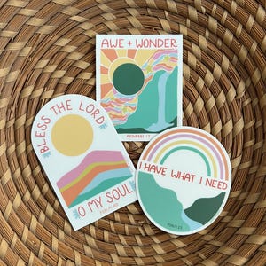 May include: Three colorful stickers with religious quotes and imagery. The first sticker is a rainbow arch with the text "Bless the Lord, O my Soul" and the scripture reference "Psalm 103". The second sticker is a rectangle with a sun, rainbow, and waterfall with the text "Awe + Wonder" and the scripture reference "Proverbs 17". The third sticker is a circle with a rainbow and the text "I have what I need" and the scripture reference "Psalm 23".