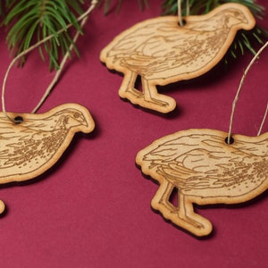 May include: Three wooden ornaments shaped like quail birds with brown and white markings. Each ornament has a string attached for hanging.