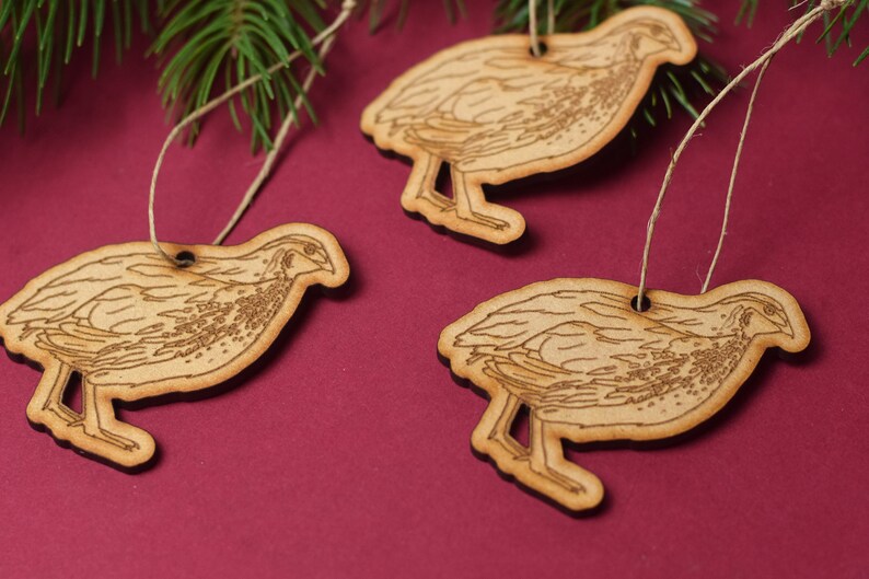 May include: Three wooden ornaments shaped like quail birds with brown and white markings. Each ornament has a string attached for hanging.