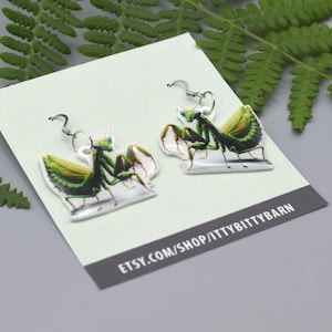 Może przedstawiać: Para zielonych kolczyków w kształcie modliszki na białej kartce z tekstem "etsy.com/shop/ittybittybarn".