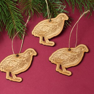 May include: Three wooden ornaments shaped like quail birds with brown twine hangers. The ornaments are on a red background.