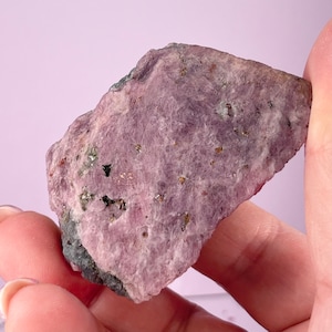 May include: A rough, purple and grey rock with flecks of gold and black throughout.