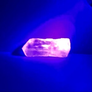 May include: A large, white, irregularly shaped rock glows a bright pink under a UV light.
