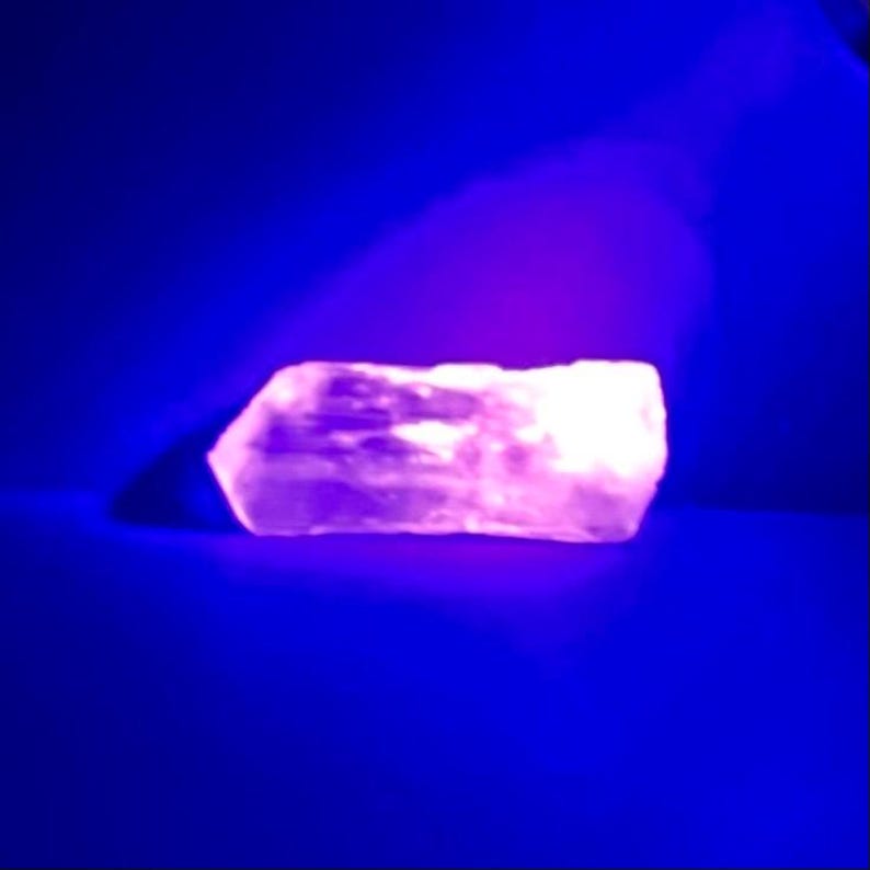 May include: A large, white, irregularly shaped rock glows a bright pink under a UV light.