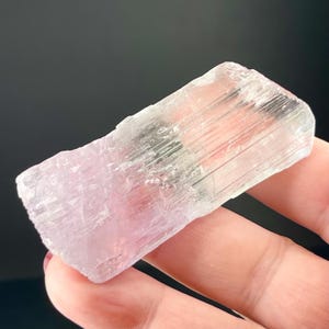 May include: A translucent, light pink selenite crystal with visible striations. The crystal is smooth and has a rectangular shape.