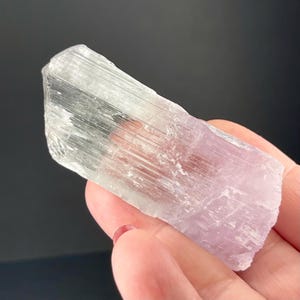 May include: A light green and pink crystal with striations. The crystal is translucent and has a smooth, polished surface.