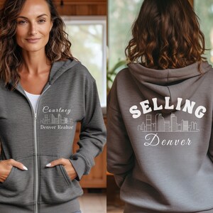 Puede incluir: Sudadera gris con cremallera y capucha con un gr&aacute;fico blanco de un horizonte de ciudad y el texto "Courtney Denver Realtor" en la parte delantera y "SELLING Denver" en la parte trasera.