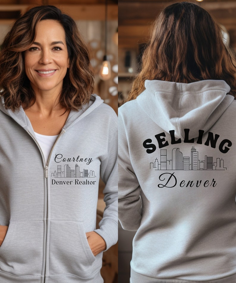Puede incluir: Una sudadera con capucha gris con cremallera y un gr&aacute;fico negro de un horizonte de ciudad y el texto "Selling Denver" en la parte posterior. La parte delantera de la sudadera tiene un gr&aacute;fico negro de un horizonte de ciudad y el texto "Courtney Denver Realtor".