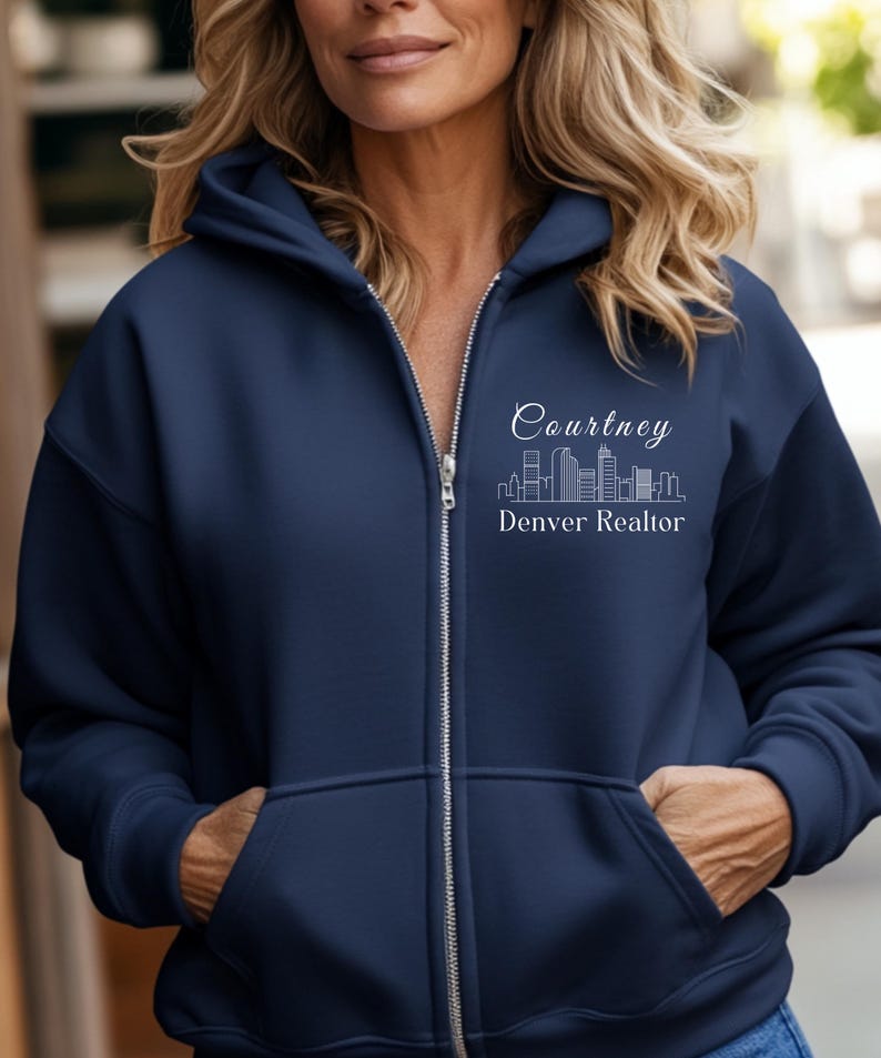 Puede incluir: Una sudadera con capucha azul marino con cremallera, con un contorno blanco de un horizonte de ciudad y el texto "Courtney Denver Realtor" en la parte delantera.