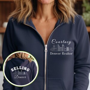 Puede incluir: Una sudadera con capucha azul marino con cremallera con un contorno blanco de un horizonte de ciudad y el texto "Courtney Denver Realtor" en la parte delantera. La parte posterior de la sudadera con capucha tiene un contorno blanco de un horizonte de ciudad y el texto "Selling Denver".