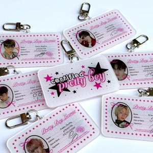 May include: A collection of clear acrylic keychains featuring photos of young men. The keychains are rectangular with rounded corners and include the text "Pretty Boy License" and "Certified Pretty Boy" in pink. Each keychain has a silver clasp.