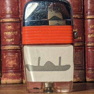 May include: A silver and red lighter with a clear plastic body. The lighter has a ship silhouette on the front and a red band around the middle.