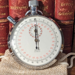 May include: A silver stopwatch with a white face and black markings. The stopwatch has a red second hand and a black minute hand. The face of the stopwatch is marked with numbers from 1 to 60. The stopwatch is labeled "ARVOR INCABLOC".
