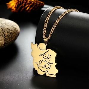 Puede incluir: Un collar dorado con un colgante con la forma de Irán. El colgante tiene una inscripción en persa. La cadena es de tipo eslabón. El fondo es negro.