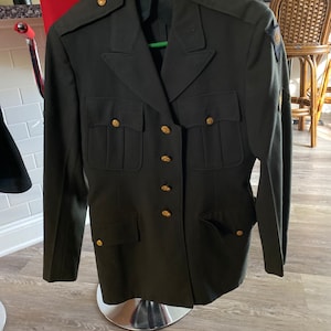 Può includere: Una giacca militare verde scuro con bottoni dorati e una toppa sulla manica.