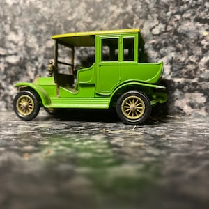 Op de afbeelding: Een groene speelgoedauto met een zwart dak en gouden wielen. De auto heeft een vierdeurs sedan carrosserie en is gemaakt van metaal.
