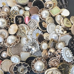 May include: A collection of assorted buttons in various colors, shapes, and sizes. The buttons are made of different materials, including metal, plastic, and fabric. Some buttons feature pearl-like accents, while others have intricate designs.