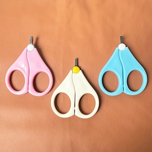 May include: Three pairs of baby nail clippers. One pair is pink, one is blue, and one is white with a yellow accent.