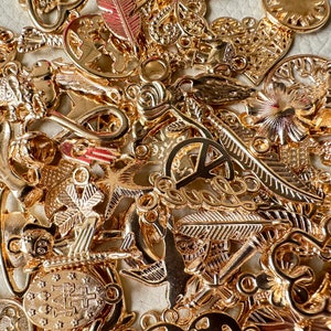 May include: A collection of gold-toned metal charms featuring various designs, including peace signs, anchors, hearts, flowers, and feathers.