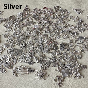 May include: A large assortment of silver charm pendants in various shapes and designs, including spiders, anchors, hearts, owls, and more. The charms are scattered on a light brown surface.