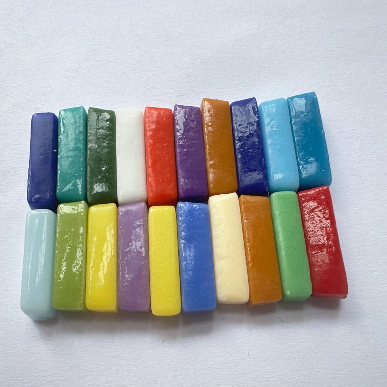May include: A collection of twenty-four rectangular blocks of modeling clay arranged in two rows. The blocks feature a glossy finish and a wide spectrum of colors including shades of blue, green, yellow, red, orange, purple, white, and cream.