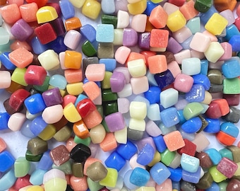 May include: A large collection of colorful, square-shaped glass tiles. The tiles are in various shades of blue, green, red, yellow, orange, and pink. The tiles are arranged in a random pattern.