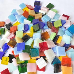 May include: A large pile of colourful square glass tiles in various shades of blue, green, red, yellow, and white. The tiles are arranged in a random pattern and are perfect for crafting projects.