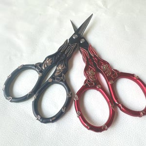 May include: Two pairs of decorative embroidery scissors. One pair is black with gold accents, and the other is red with gold accents. Both have ornate handles and pointed blades, ideal for detailed craftwork.