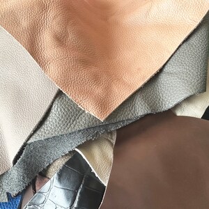 May include: A close-up of a stack of different colored leather swatches. The swatches are arranged in a fan shape, with the lightest color on top and the darkest color on the bottom. The colors are brown, gray, and black.