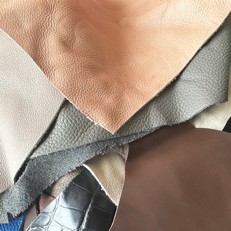 May include: A close-up of a stack of different colored leather swatches. The swatches are arranged in a fan shape, with the lightest color on top and the darkest color on the bottom. The colors are brown, gray, and black.
