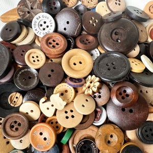 Puede incluir: Una colección de botones surtidos en varios colores, formas y tamaños. Los botones están hechos de madera, plástico y metal. Algunos botones tienen un diseño floral, mientras que otros tienen un diseño simple. Los botones están dispuestos en un patrón aleatorio.