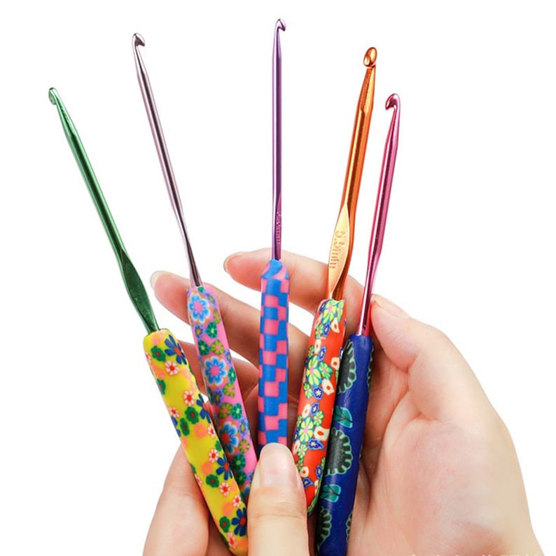 May include: Five colourful crochet hooks with different coloured handles and metal tips. The handles are decorated with floral and geometric patterns.