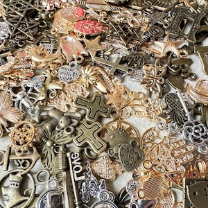May include: A large collection of mixed metal charms in gold, silver, and bronze tones. The charms feature various designs, including crosses, stars, hearts, butterflies, and keys. Some charms have words on them, such as "Made with Love" and "Long".