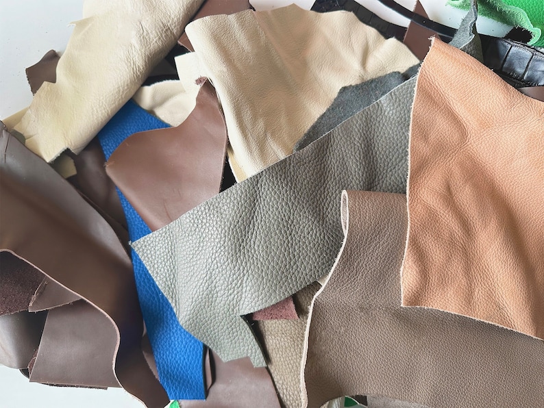 May include: A collection of leather scraps in various colors, including brown, beige, gray, and blue. The leather is arranged in a random pattern, showing the different textures and shades.