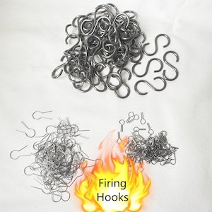 Könnte beinhalten: Ein großer Haufen silberner Metallhaken, mit einem kleineren Haufen silberner Metallhaken im Hintergrund. Der Text "Firing Hooks" ist in orangefarbenen und gelben Flammen geschrieben.