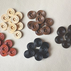 May include: Assortment of wooden buttons in various sizes and colors, including brown, beige, and cream. The buttons are arranged in groups of three, with each group featuring a different color scheme.
