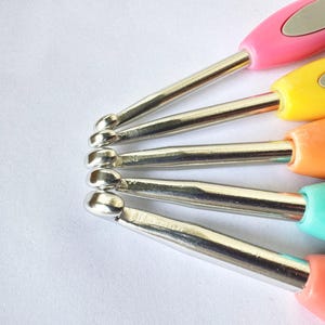 May include: A set of five colourful crochet hooks with silver metal tips. The hooks are arranged in a fan shape, with the handles facing up.