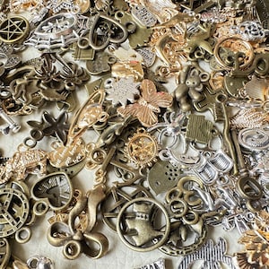 May include: A large collection of mixed metal charms in silver, gold, and bronze tones. The charms feature various designs, including hearts, stars, butterflies, and keys. Some charms have words or phrases on them, such as "Love you" and "Be Strong".