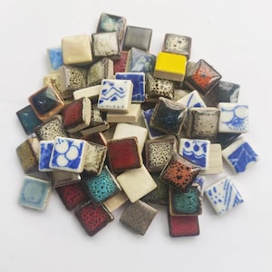 May include: A collection of small, square ceramic tiles in various colours and patterns. The tiles are approximately 2.5 cm in size and feature a range of designs, including geometric patterns, floral motifs, and abstract designs.