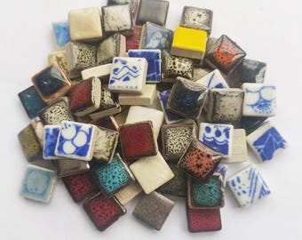 Può includere: Una collezione di piccole piastrelle quadrate in ceramica di vari colori e motivi. Le piastrelle sono di circa 2,5 cm di lato e presentano una varietà di disegni, tra cui motivi geometrici, motivi floreali e disegni astratti.