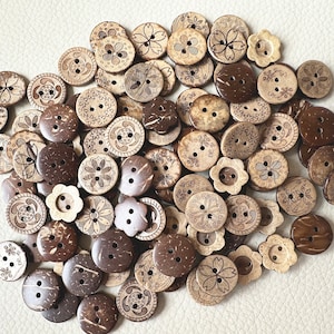 Könnte beinhalten: Eine Sammlung brauner Kokosnuss-Knöpfe mit verschiedenen floralen und geometrischen Mustern. Die Knöpfe sind auf einer weißen Oberfläche verstreut.