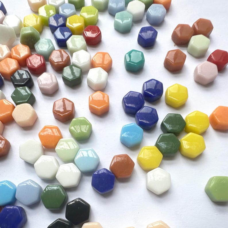 Pu&ograve; includere: Una collezione di piccole tessere di vetro esagonali in un'ampia variet&agrave; di colori solidi, tra cui rosso, blu, giallo, verde, arancione, bianco, nero e varie tonalit&agrave; pastello. Ogni tessera ha una finitura liscia, lucida e uniforme.